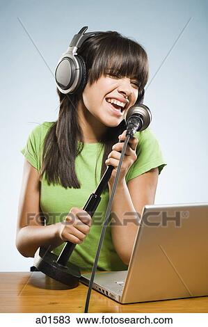 Young woman recording into a microphone with headphones and a laptop View Large Photo Image Stock Image - Young woman recording into a microphone with headphones and a laptop. Fotosearch