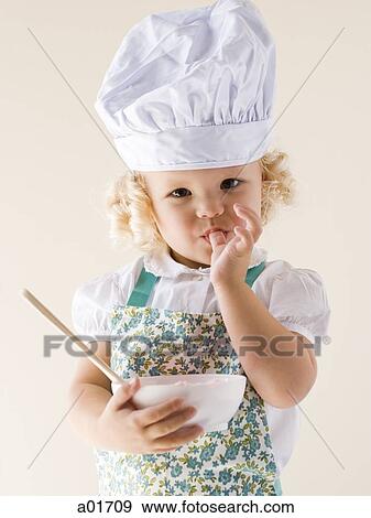 Stock Photo - Little girl wearing a chef's hat and holding a bowl.. Fotosearch