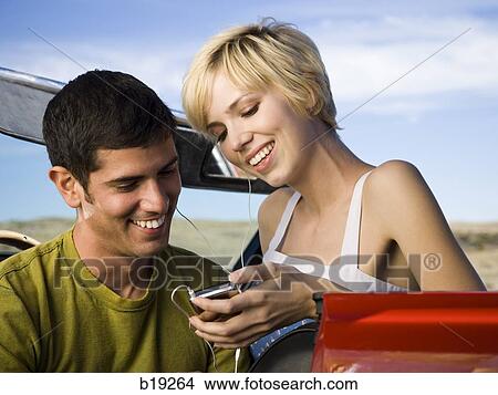 Picture - man and woman next to a red convertible. Fotosearch
