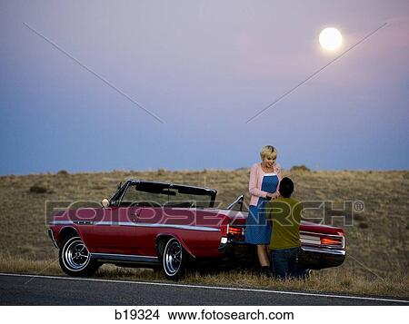 Picture - man and woman next to a red convertible. Fotosearch