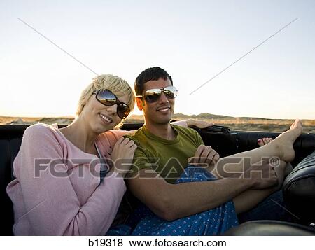 Stock Photo - man and woman next to a red convertible. Fotosearch