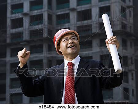 Man in suit on a construction job site with plans in hand. View Large Photo Image Picture - Man in suit on a construction job site with plans in hand.. Fotosearch