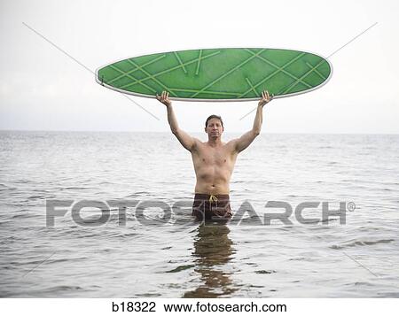 Man in the ocean holding a surfboard. View Large Photo Image Stock Image - Man in the ocean holding a surfboard.. Fotosearch