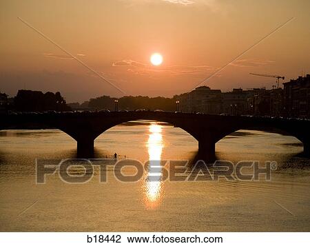 Man rowing on a body of water with a bridge and setting sun in the background. View Large Photo Image Stock Image - Man rowing on a body of water with a bridge and setting sun in the background.. Fotosearch