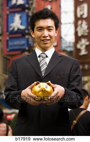 Stock Photo - Man standing on a city street with a piggy bank.. Fotosearch