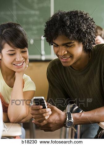 Stock Image - Students playing with cell phone in a classroom.. Fotosearch