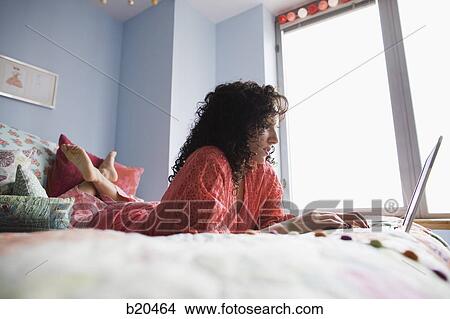 woman lying on a bed with a notebook computer View Large Photo Image Picture - woman lying on a bed with a notebook computer. Fotosearch