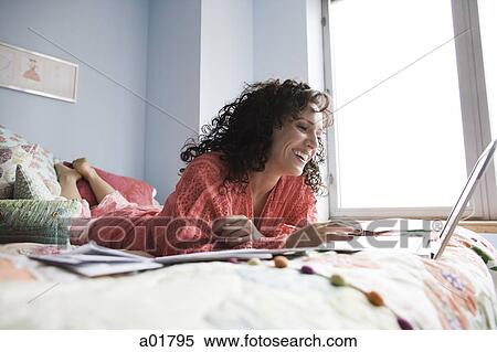 woman lying on a bed with a notebook computer View Large Photo Image Stock Photography - woman lying on a bed with a notebook computer. Fotosearch