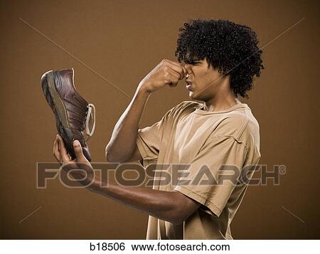 young man in a brown shirt holding a shoe and his nose. View Large Photo Image Stock Photograph - young man in a brown shirt holding a shoe and his nose.. Fotosearch