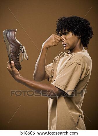 young man in a brown shirt holding a shoe and his nose. View Large Photo Image Stock Photography - young man in a brown shirt holding a shoe and his nose.. Fotosearch