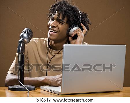 young man in a brown shirt on a laptop with headphones and a microphone. View Large Photo Image Stock Photo - young man in a brown shirt on a laptop with headphones and a microphone.. Fotosearch