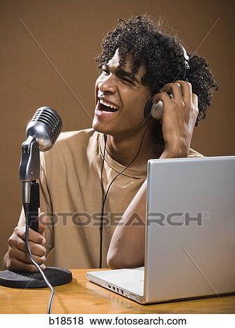 young man in a brown shirt on a laptop with headphones and a microphone. View Large Photo Image Stock Photo - young man in a brown shirt on a laptop with headphones and a microphone.. Fotosearch