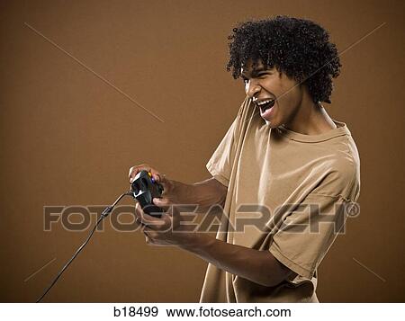 young man in a brown shirt playing a video game. View Large Photo Image Stock Photo - young man in a brown shirt playing a video game.. Fotosearch
