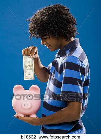 Stock Image - young man putting money in a piggy bank.. Fotosearch