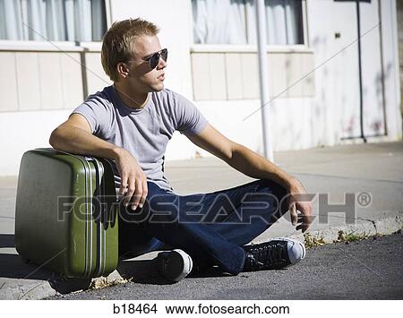 Young man sitting with a suitcase. View Large Photo Image Picture - Young man sitting with a suitcase.. Fotosearch