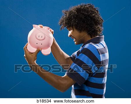 young man trying to get money out of a piggy bank. View Large Photo Image Picture - young man trying to get money out of a piggy bank.. Fotosearch