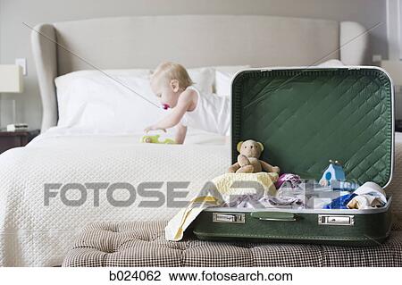 Stock Image - baby crawling bed next to an open suitcase. Fotosearch