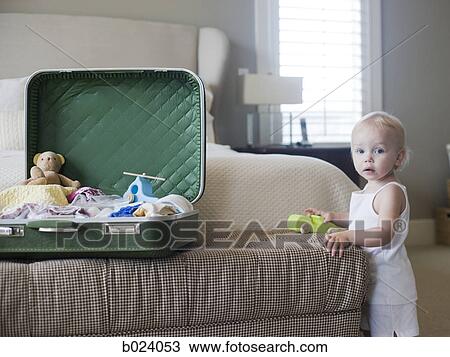 Stock Image - baby girl standing next to open suitcase. Fotosearch