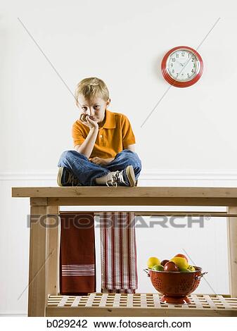 Stock Image - boy sitting on a kitchen table. Fotosearch