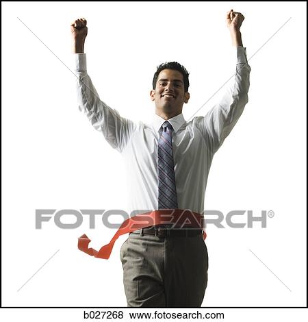 Stock Photo - businessman crossing a finish line of a red ribbon with arms raised in the air triumphantly. Fotosearch