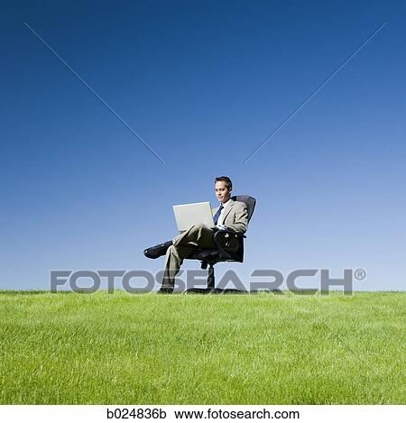 Stock Image - businessman using his laptop in a grassy field. Fotosearch