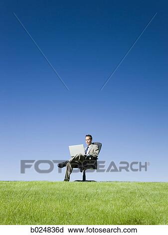 Stock Image - businessman using his laptop in a grassy field. Fotosearch