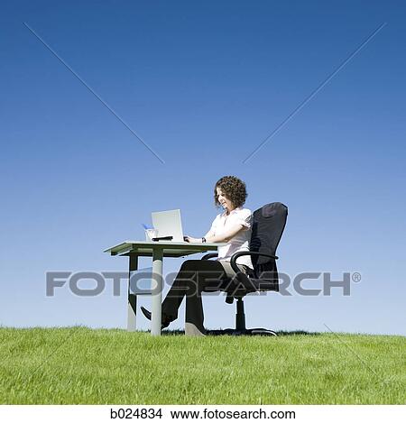 Picture - businesswoman at her desk in a grassy field. Fotosearch