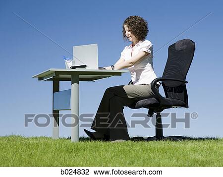 Stock Image - businesswoman at her desk in a grassy field. Fotosearch