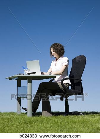 Stock Image - businesswoman at her desk in a grassy field. Fotosearch