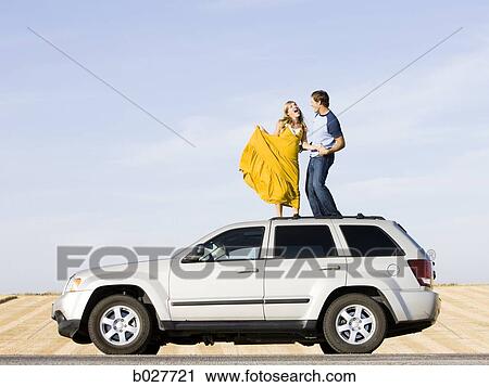 Stock Image - couple on the roof of their car on the side of the road. Fotosearch