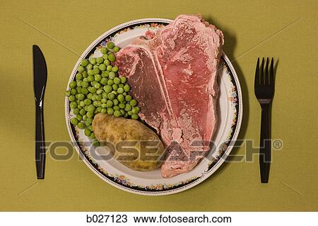 Stock Image - frozen uncooked steak being served on a plate. Fotosearch