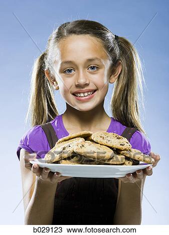 Stock Image - girl looking at the camera holding a plate of chocolate chip cookies. Fotosearch