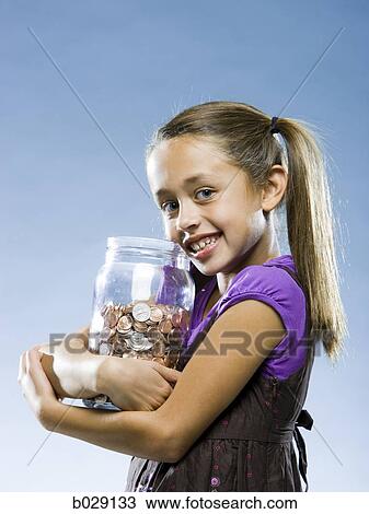 Stock Image - girl looking at the camera holding a jar of coins. Fotosearch