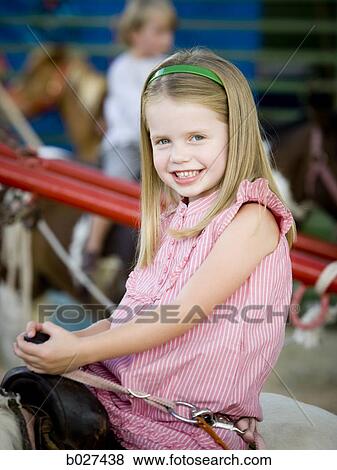 Stock Photo - girl sitting on a pony at the carnival. Fotosearch