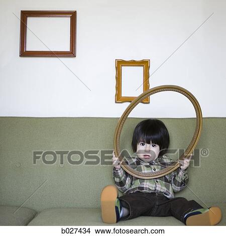 little boy on a couch holding a picture frame View Large Photo Image Picture - little boy on a couch holding a picture frame. Fotosearch