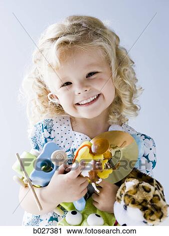 Stock Image - little girl holding an armful of her toys. Fotosearch