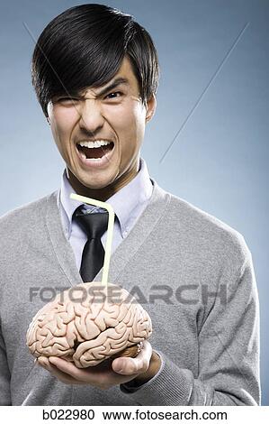 Stock Image - man holding a brain with a drinking straw sticking out of it. Fotosearch