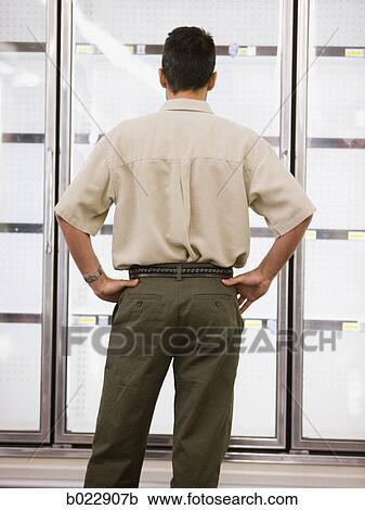 Stock Image - man looking into empty refrigerators at market. Fotosearch