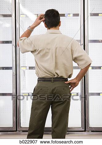 Stock Photo - man looking into empty refrigerators at market. Fotosearch
