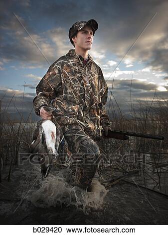 Stock Image - man out hunting carrying back a duck. Fotosearch