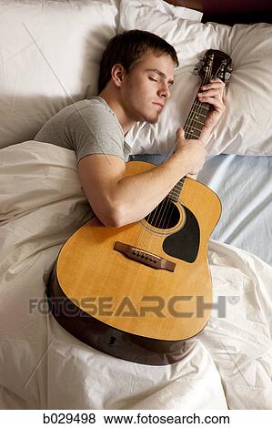 Stock Photo - man sleeping with his guitar. Fotosearch
