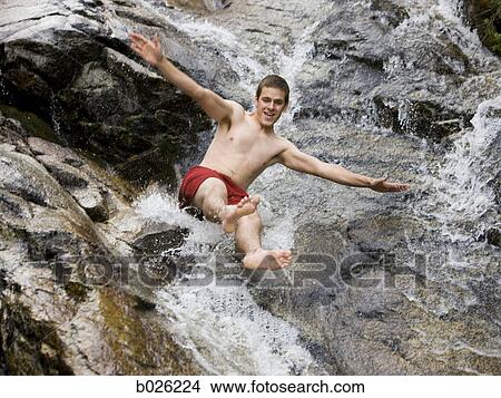 Picture - man sliding down a rock waterslide. Fotosearch
