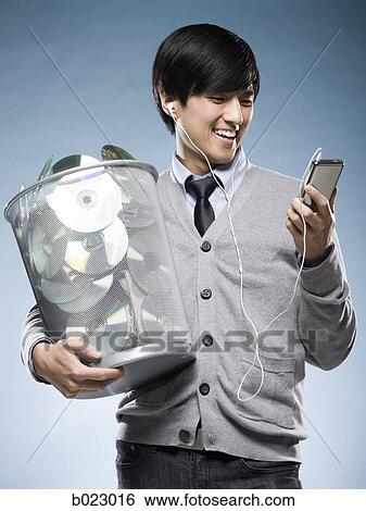 Stock Photograph - man with a trash can full of cd's and holding an iPod. Fotosearch