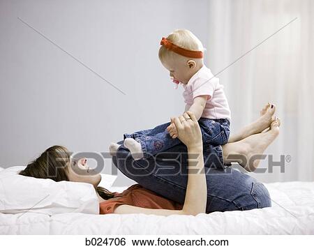 Stock Photograph - mother and baby girl lying on a bed. Fotosearch