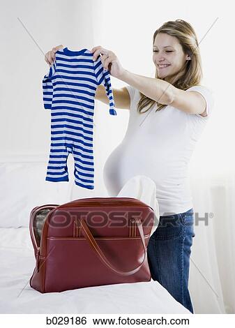 Stock Photograph - pregnant woman holding up baby clothing. Fotosearch