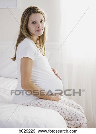 Stock Image - pregnant woman sitting on a bed. Fotosearch