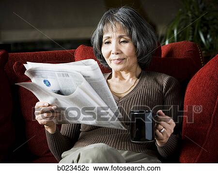 Stock Image - senior woman reading a newspaper on the couch. Fotosearch