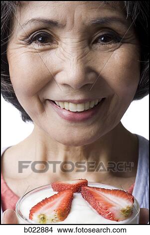 Picture - senior woman with a bowl of cereal and strawberries. Fotosearch
