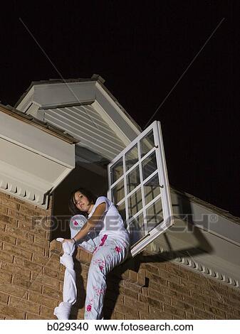 Stock Image - teenager climbing out of her bedroom window. Fotosearch