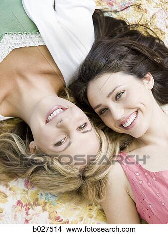 Picture - two women lying down on a floral print blanket outside. Fotosearch